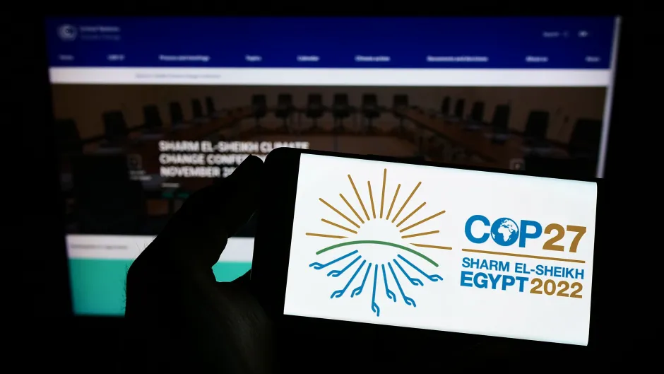 Handydisplay mit Logo der COP27 vor verschwommenem Computerbildschirm